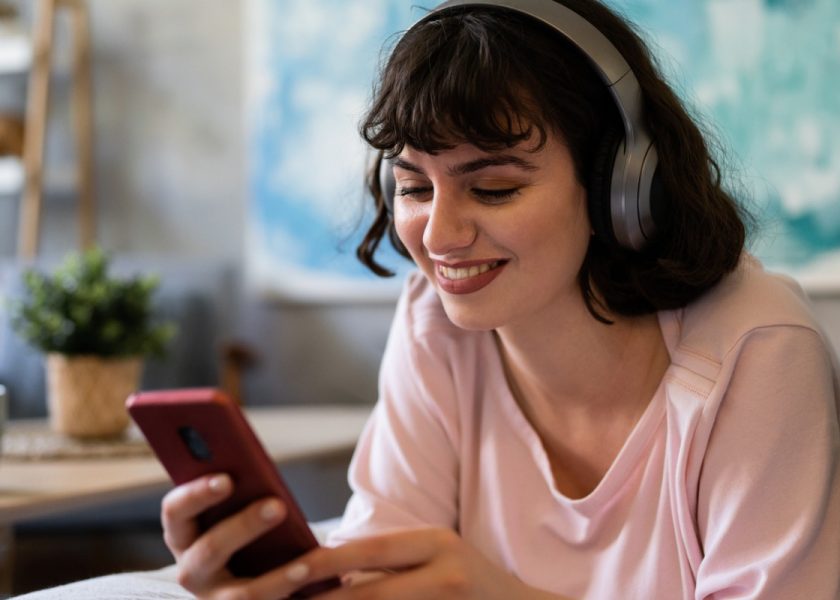 caucasian-woman-lying-on-the-sofa-using-mobile-phone-while-listening-picture-id1408269768