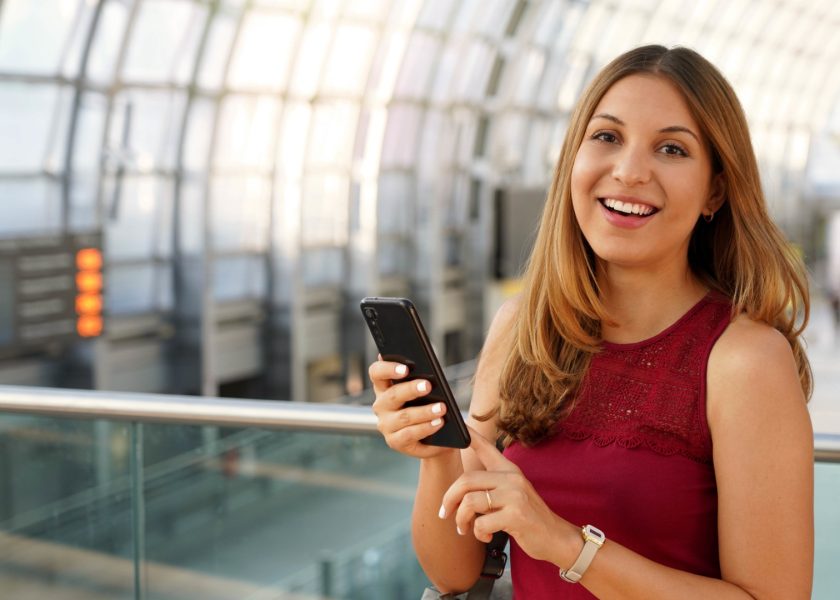 giovane-donna-sorridente-che-usa-il-telefono-cellulare-mentre-si-trova-in-piedi-sulla.jpg_s=1024×1024&w=is&k=20&c=QYFGDBbliZ_MFeyQ5yXQBIR515XkoTY072nf7YVPAZE=